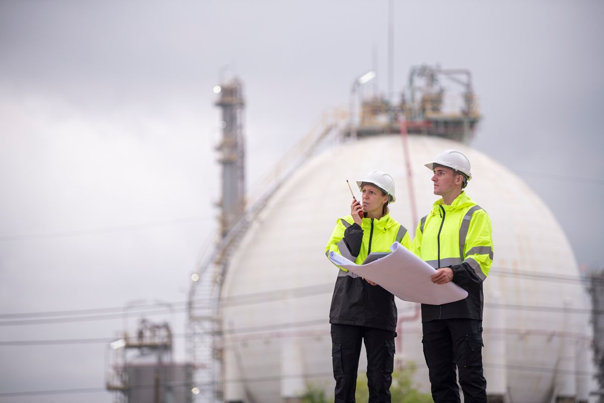 Two engineers in hard hats reviewing drawings at a refinery